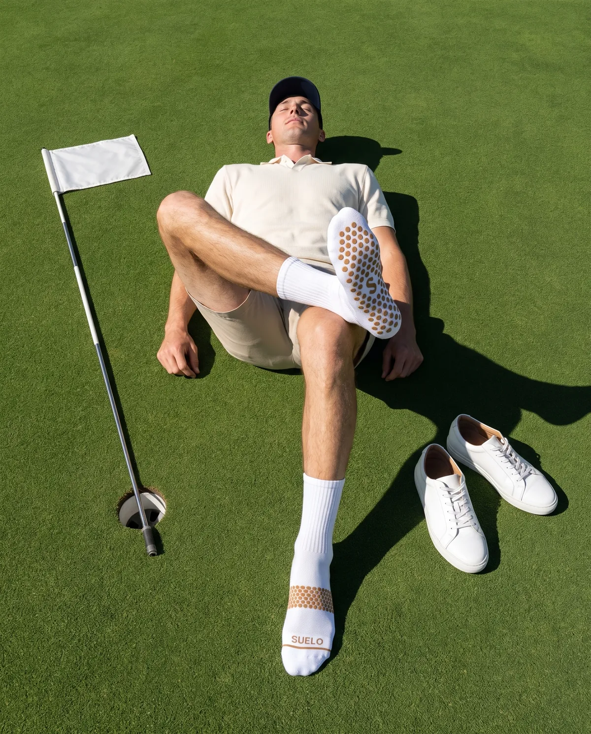 A golfer lies on a green, one foot crossed over a knee so the sock's grip sole faces up.